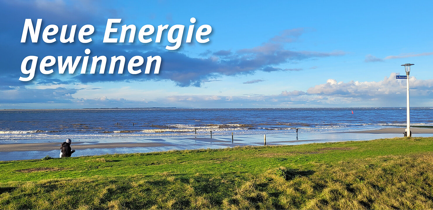 Grasbewachsene Düne, dahinter zwei Personen am Strand, dahinter Nordsee unter blauem Himmel mit Wolken. Die Überschrift auf dem Bild lautet: Neue Energie gewinnen.